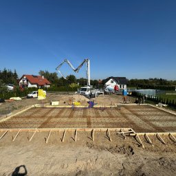 Sanadom Marcin Linowiecki - Zbrojenie przygotowane do wylania fundamentów pod budowę domu jednorodzinnego, widoczna pompa do betonu i ekipa budowlana w tle.