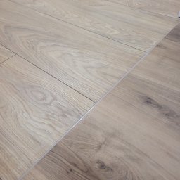 Mateusz Hołub APPLINO - Ułożone panele podłogowe z widocznymi łączeniami i delikatnym wzorem drewna.