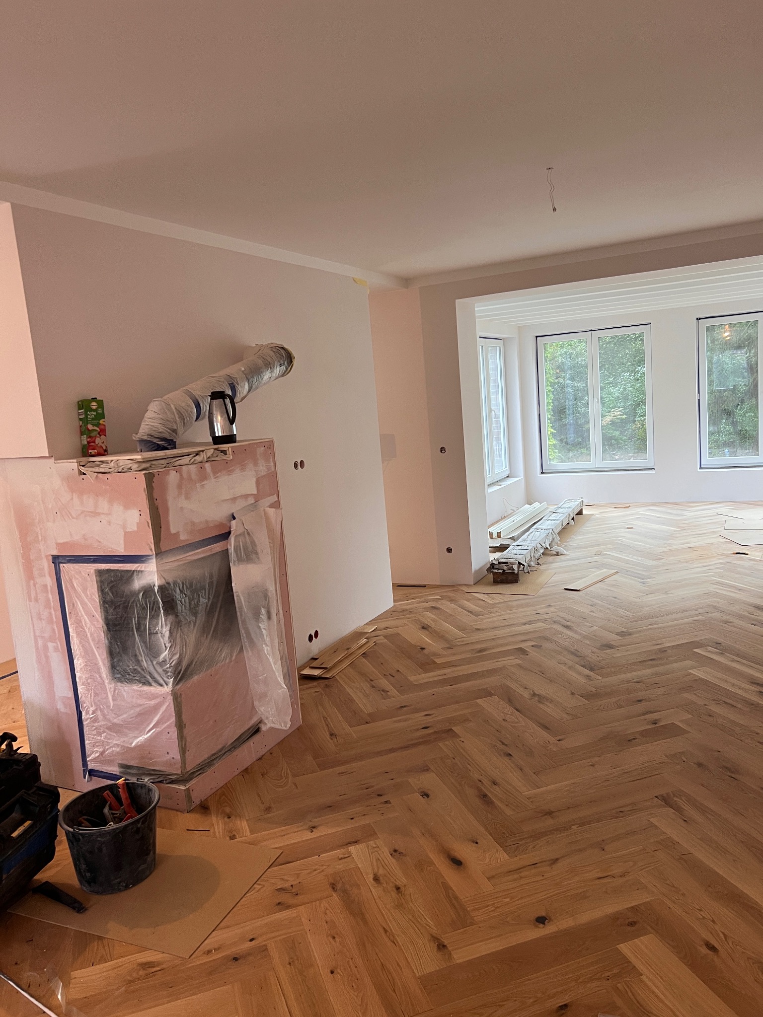 Wnętrze w trakcie remontu: ułożony parkiet w jodełkę, zabezpieczony kominek w folii, przygotowane listwy przypodłogowe przy oknie.