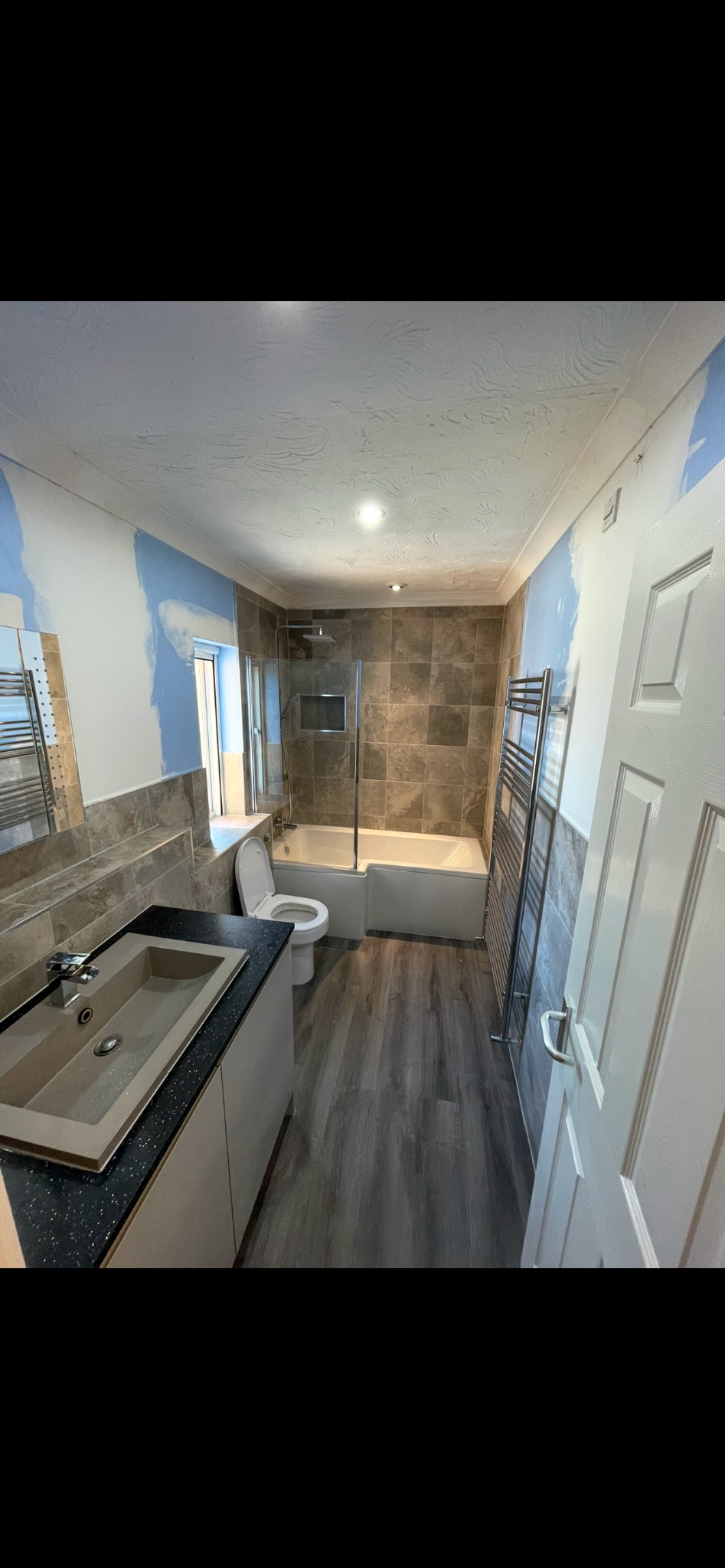 Wyremontowana łazienka z wanną z parawanem, umywalką nablatową na szafce z czarnym blatem, grzejnikiem drabinkowym i drewnopodobną podłogą, ściany częściowo pomalowane na biało z niebieskimi akcentami