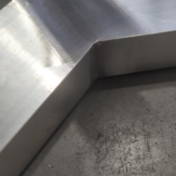 Paweł Weiner - Fragment balustrady nierdzewnej z widocznym spawanym narożnikiem, leżący na betonowej posadzce.