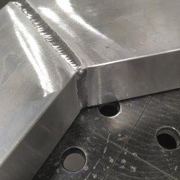 Paweł Weiner - Spoina na aluminiowym profilu kątowym, wykonana metodą spawania, widoczna na perforowanym stole spawalniczym.