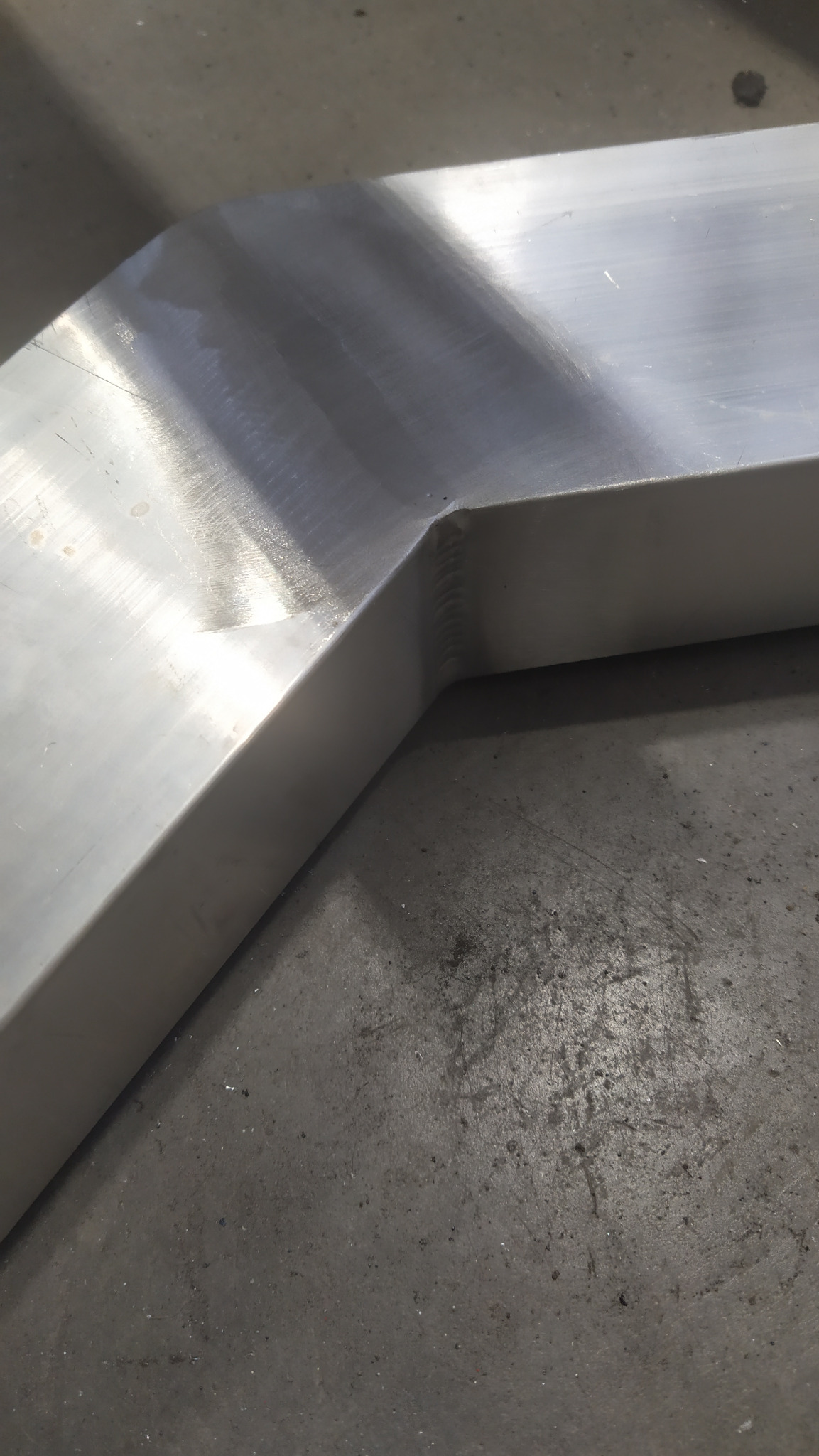 Fragment balustrady nierdzewnej z widocznym spawanym narożnikiem, leżący na betonowej posadzce.