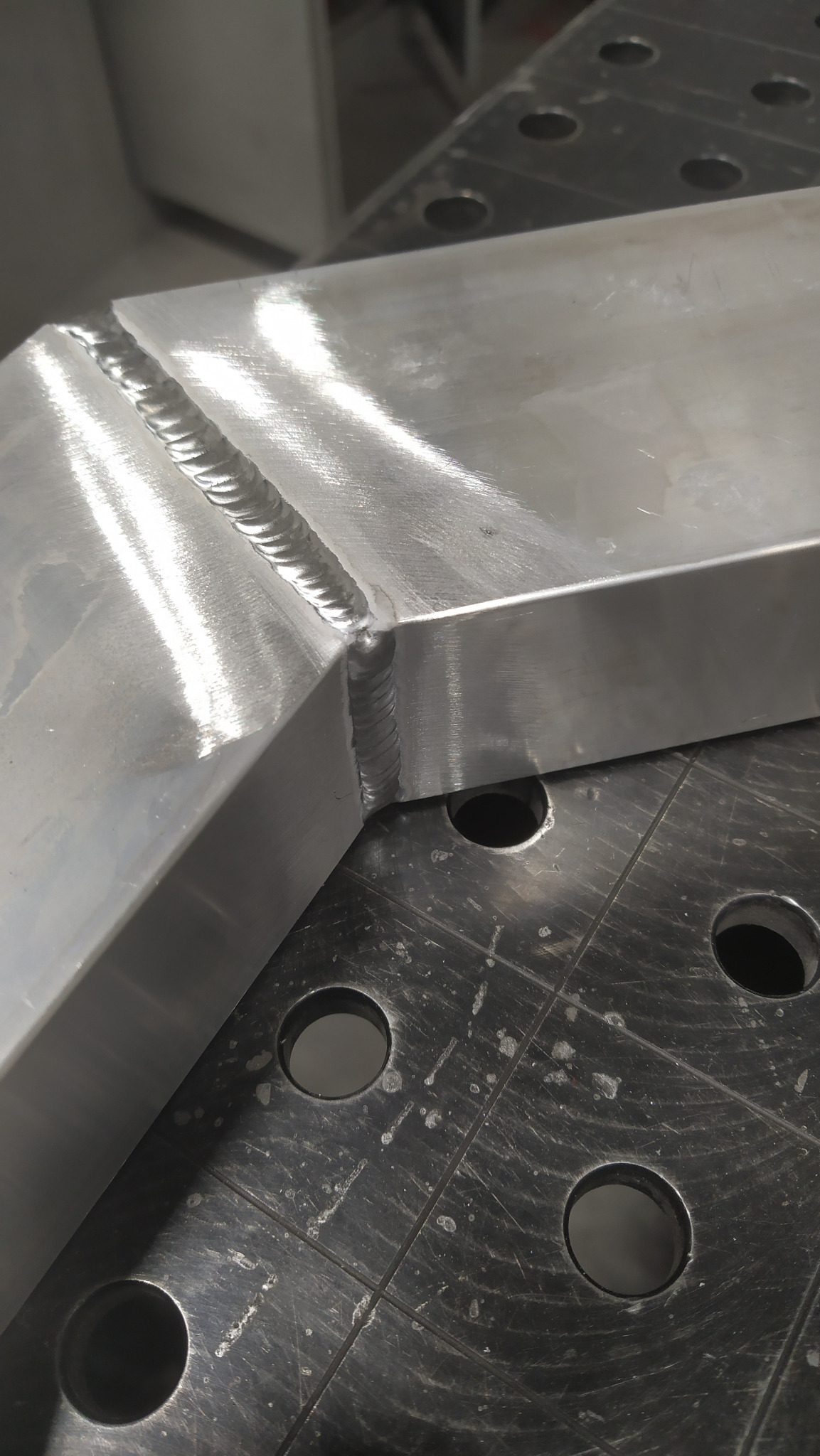 Spoina na aluminiowym profilu kątowym, wykonana metodą spawania, widoczna na perforowanym stole spawalniczym.