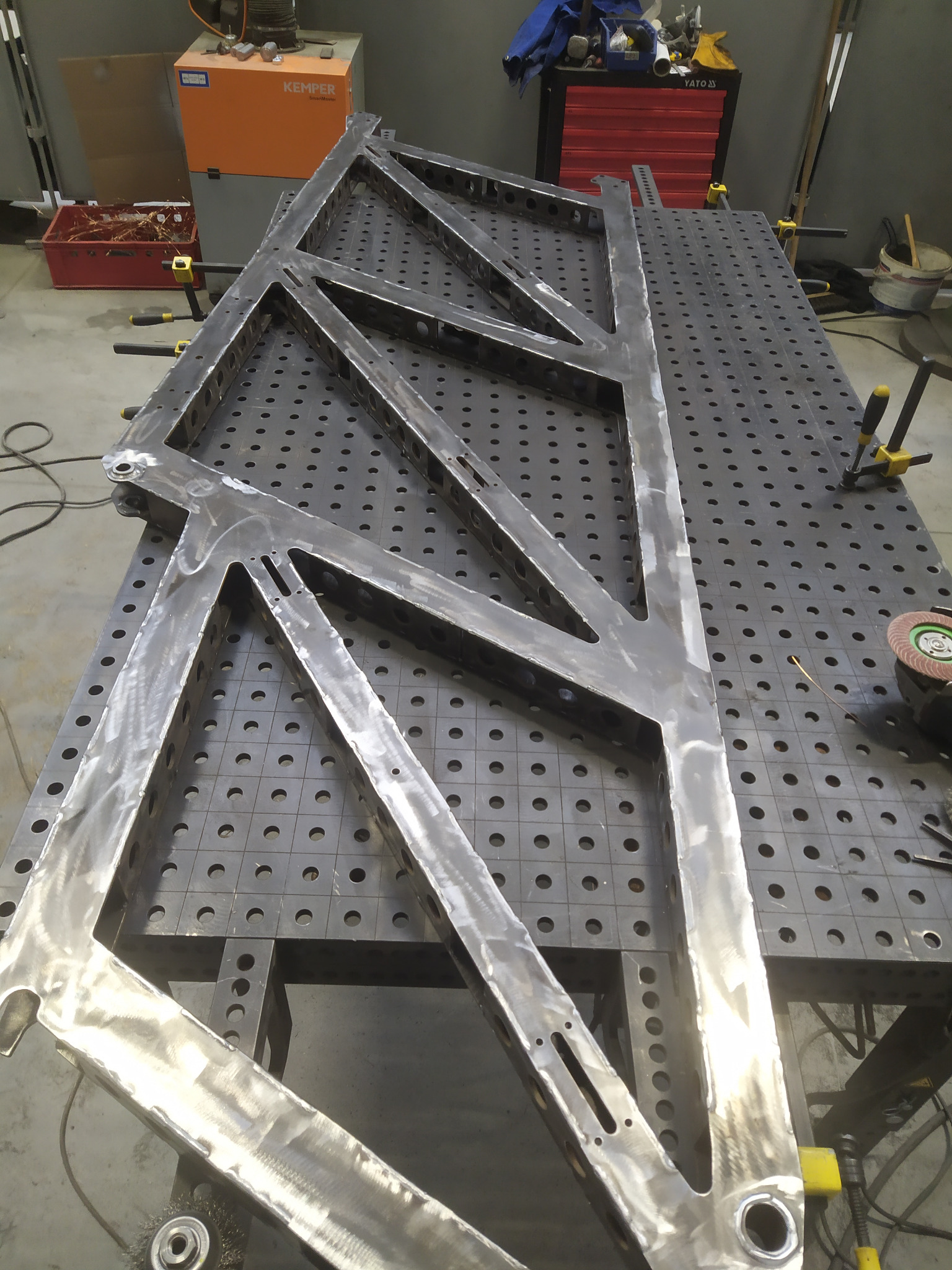 Stalowa konstrukcja kratowa na perforowanym stole spawalniczym, widoczne ślady obróbki i mocowania zaciskami.
