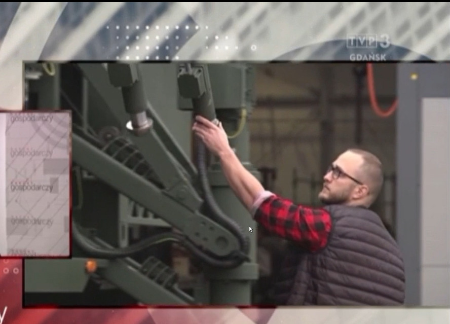 Mężczyzna w okularach i koszuli w kratę sprawdza połączenia rur w konstrukcji metalowej w hali produkcyjnej.