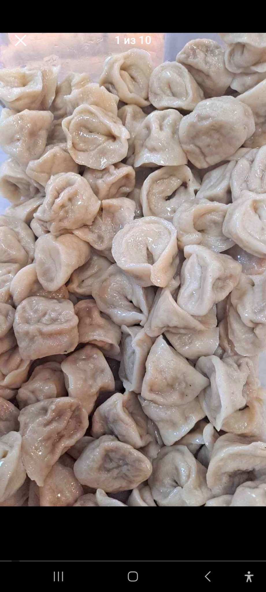 Bliksko ujęcie dużej ilości ugotowanych pierogów, lekko błyszczących, ułożonych jeden na drugim w przezroczystym pojemniku.