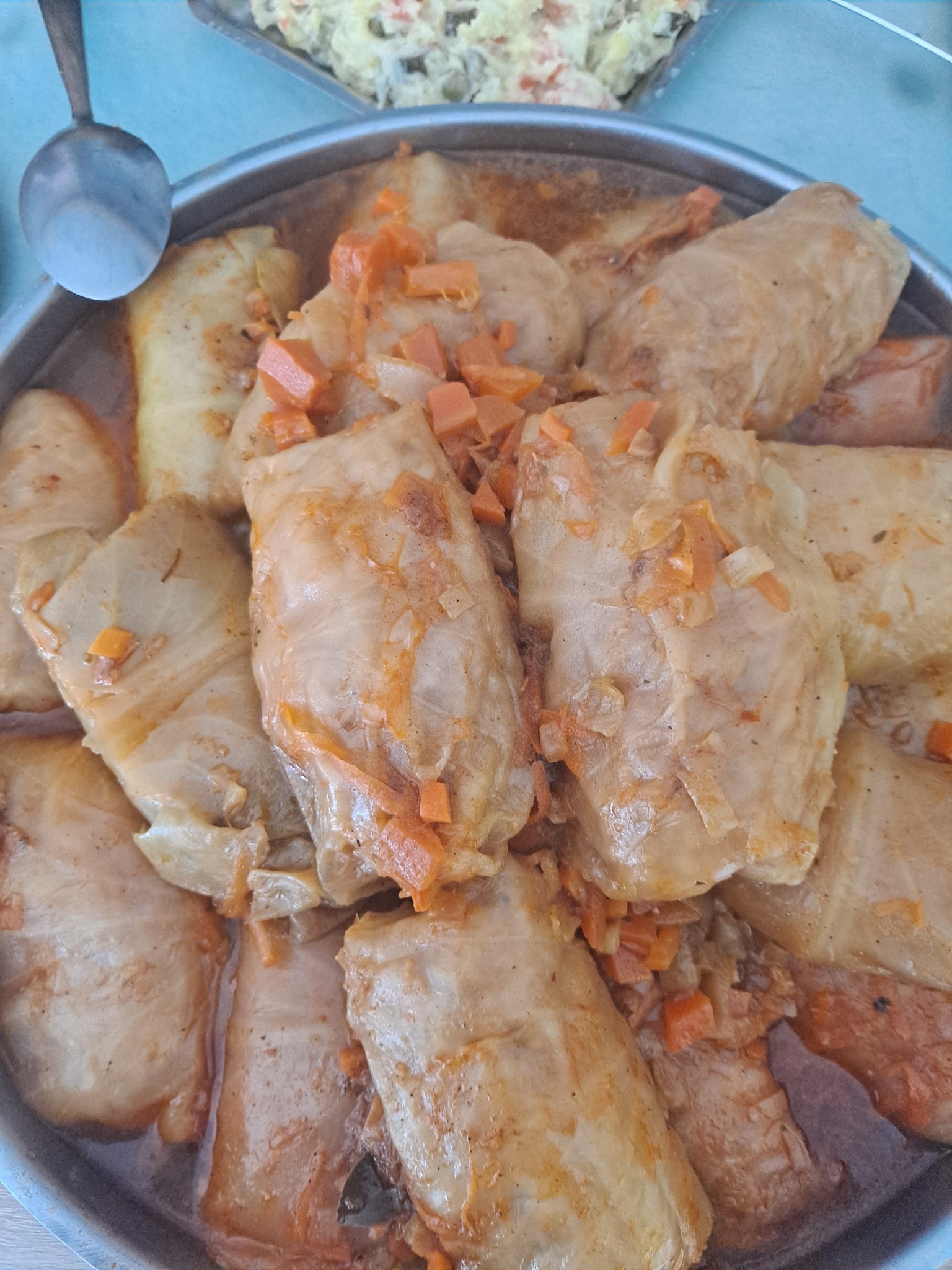 Gołąbki w sosie pomidorowym z marchewką, podane w srebrnej metalowej misce, widoczna łyżka w tle i sałatka jarzynowa.