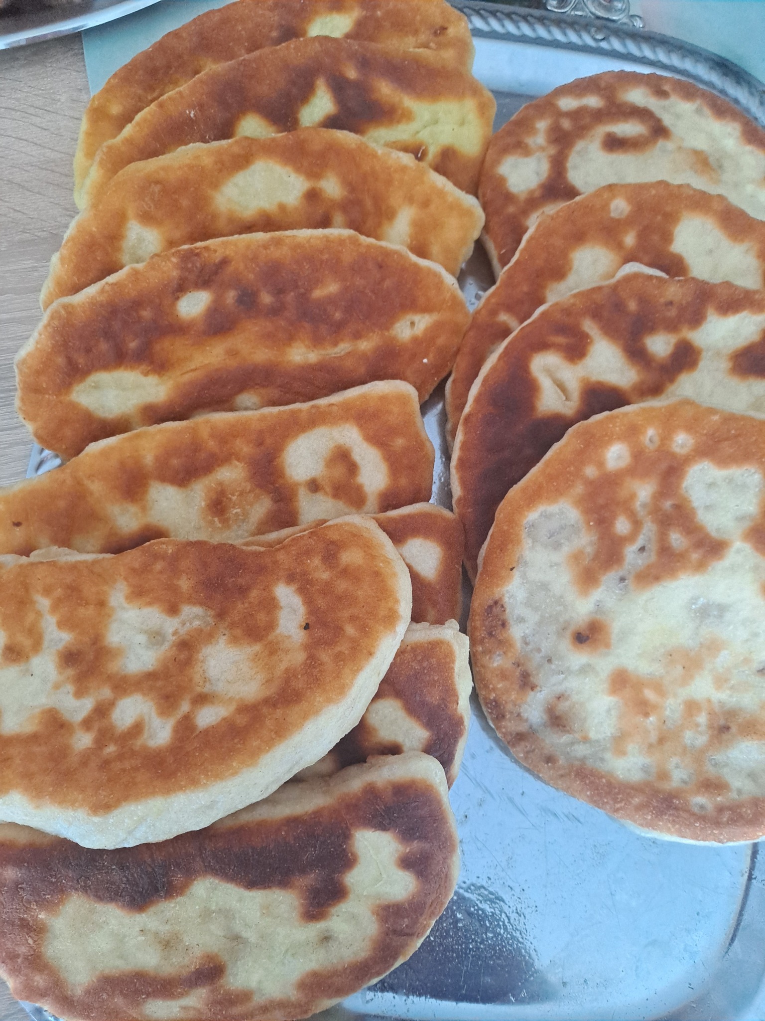 Smażone pierogi z farszem na srebrnej tacy, część w kształcie półksiężyca, część okrągła, z widocznymi brązowymi plamami po smażeniu.