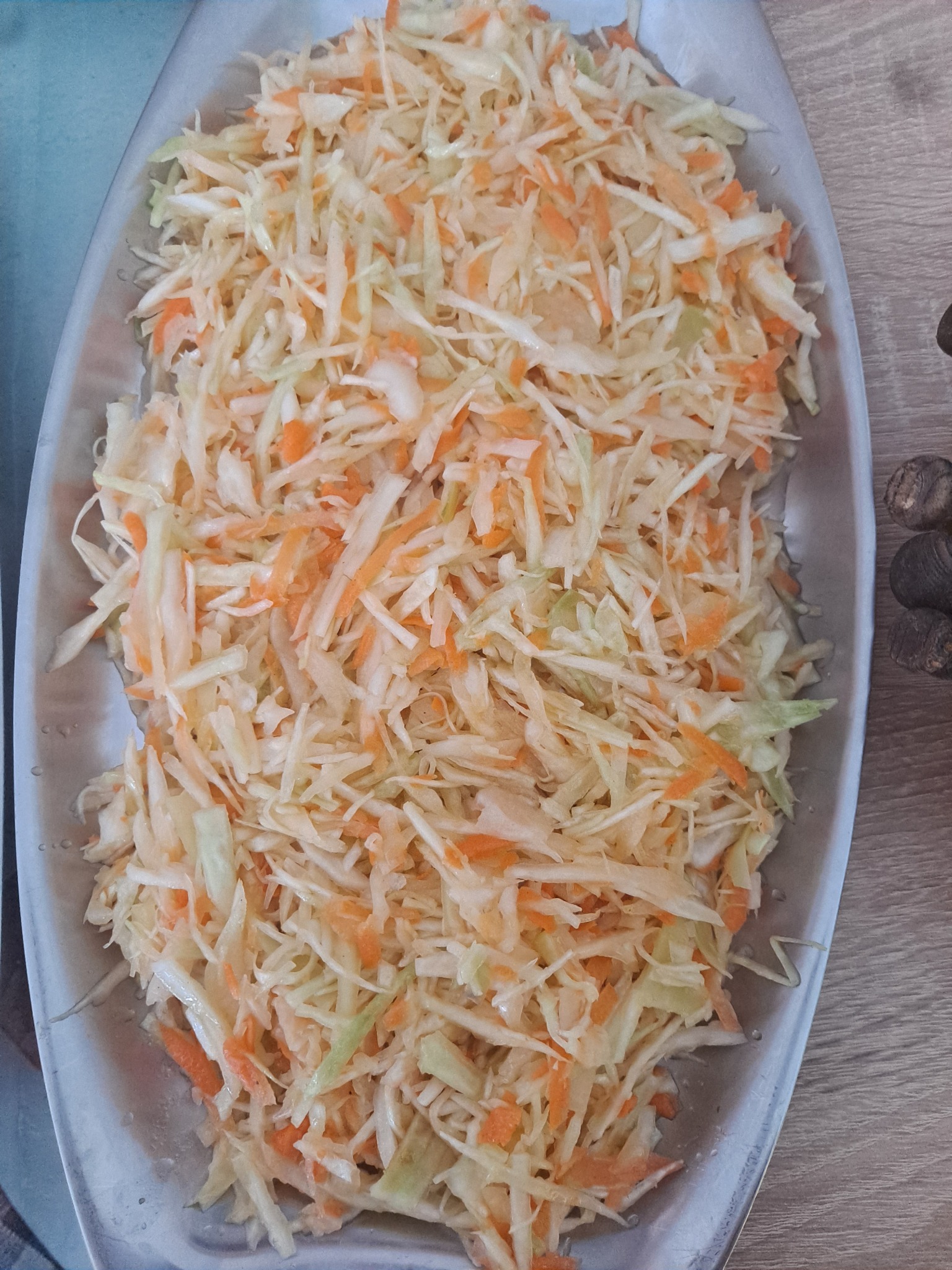 Świeżo poszatkowana surówka z białej kapusty i marchwi, ułożona na srebrnej, owalnej tacy, częściowo widoczna na drewnianym blacie.