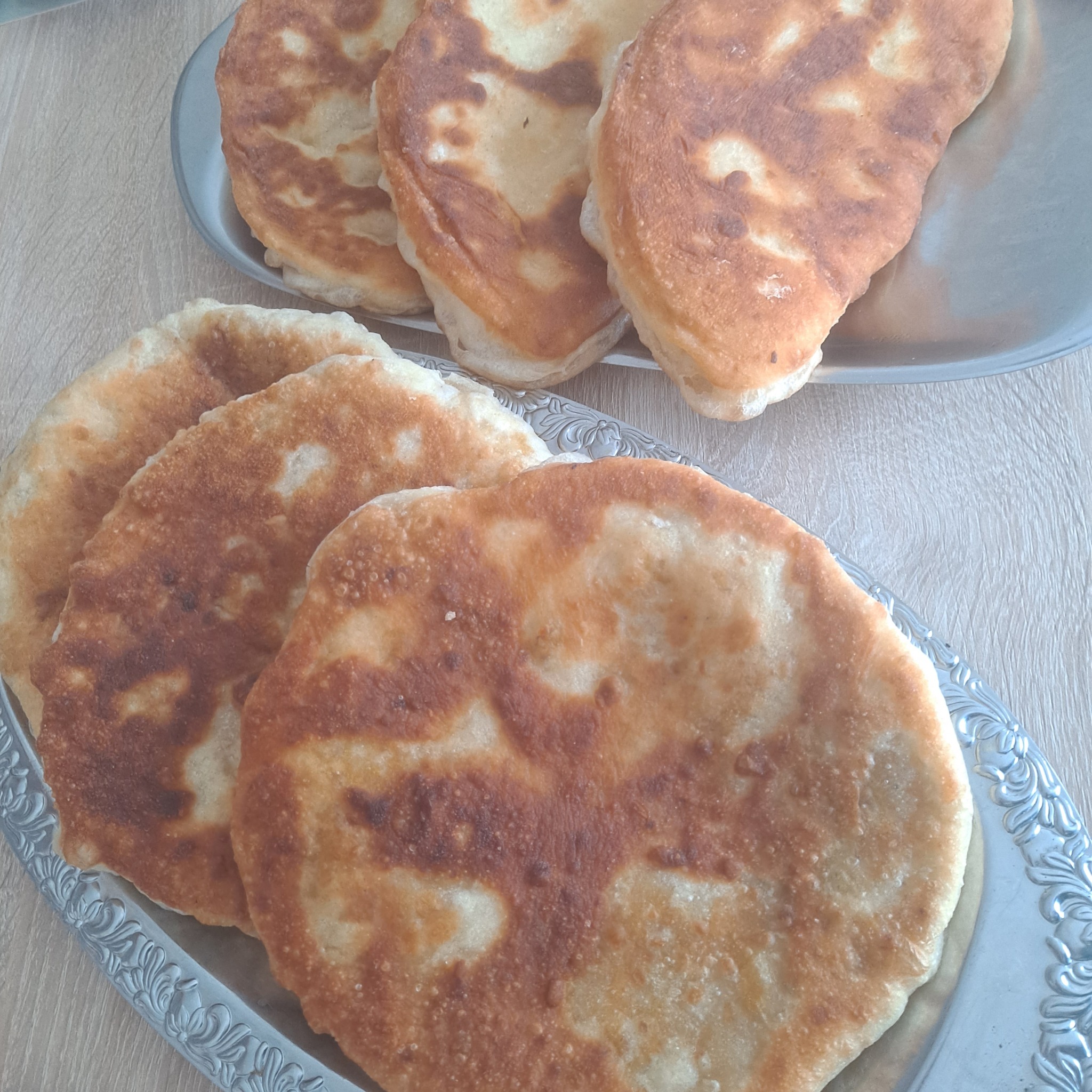 Domowe, smażone placki na srebrnych, zdobionych tacach, ustawione na drewnianym stole.