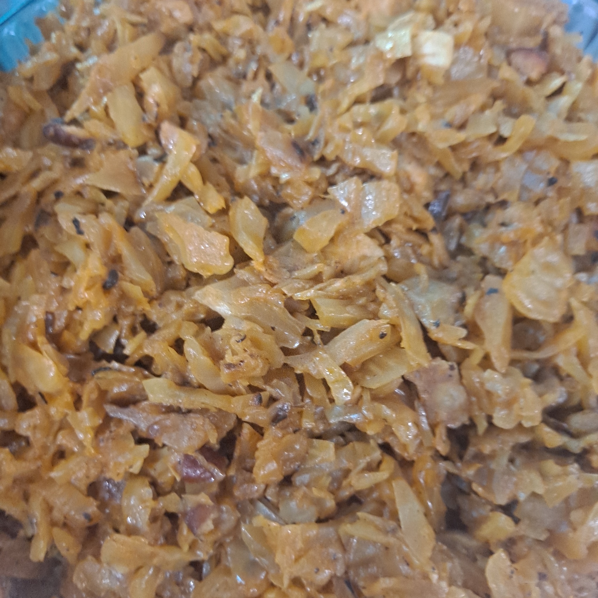 Bliski plan duszonej kapusty z przyprawami, widoczne kawałki cebuli i ciemne ziarna pieprzu.