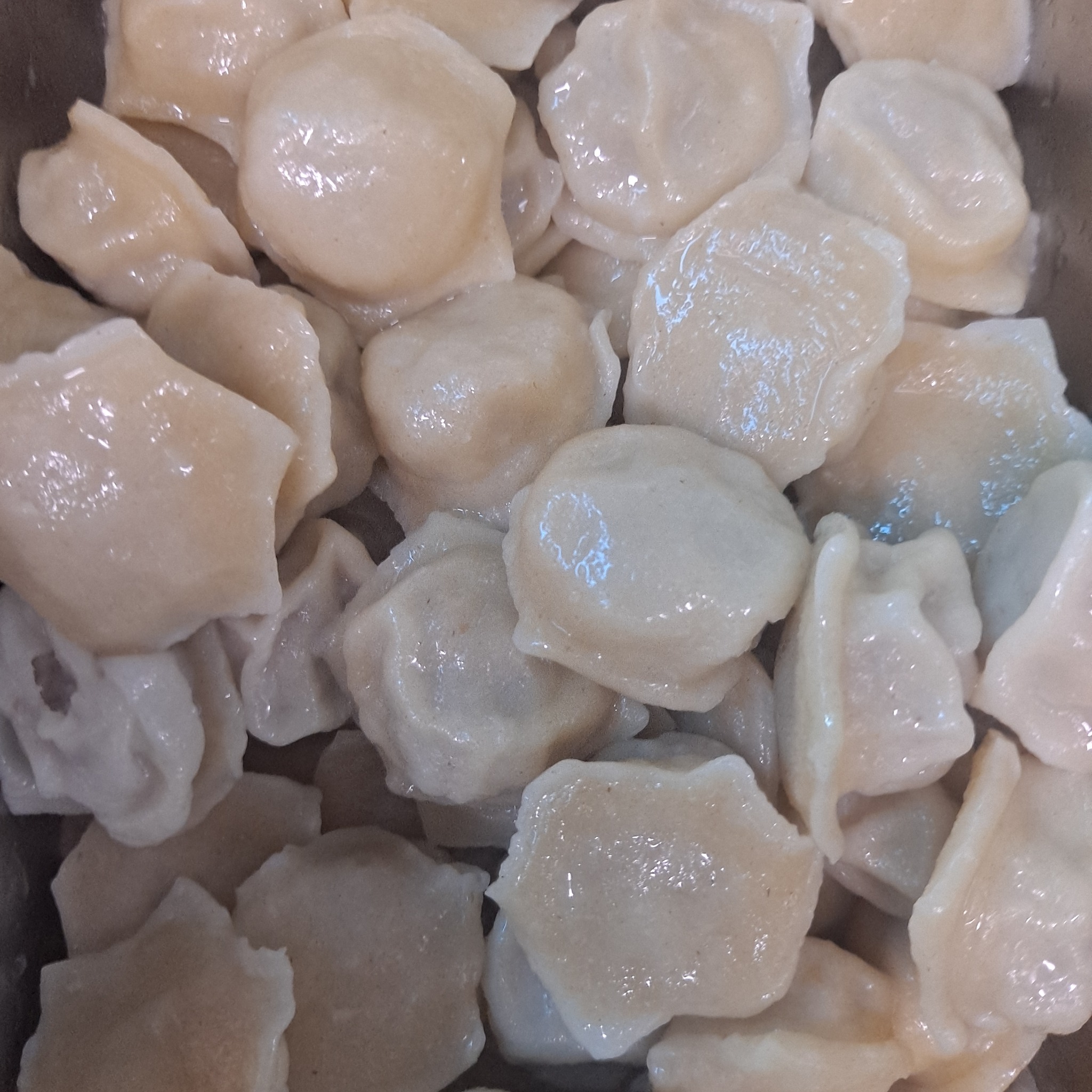 Bliski kadr pierogów w Świdnicy, z widoczną delikatną, błyszczącą skórką i jasnym farszem, ułożonych jeden na drugim w metalowym pojemniku.