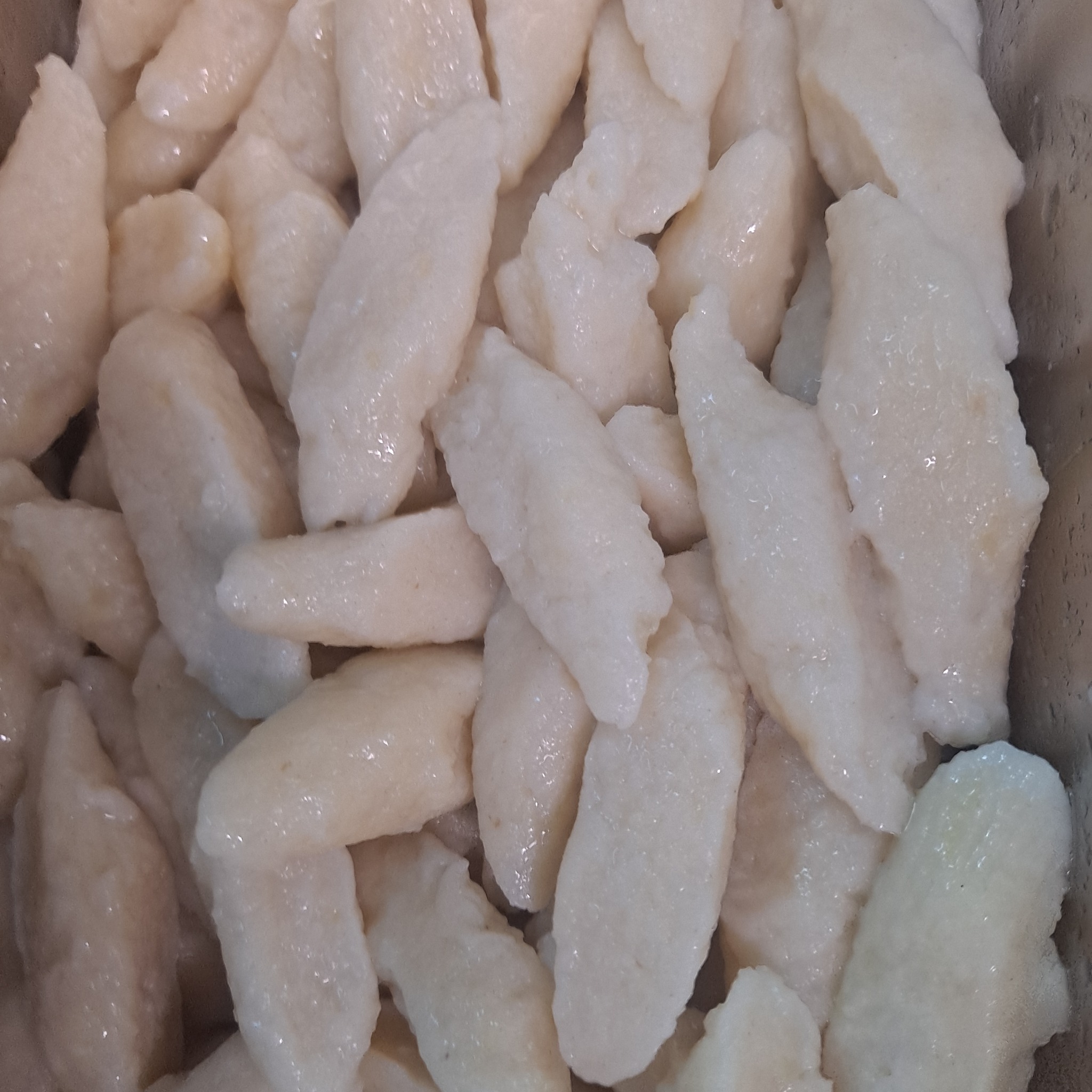 Kopytka ziemniaczane, lekko błyszczące, ułożone w pojemniku, gotowe do podania.