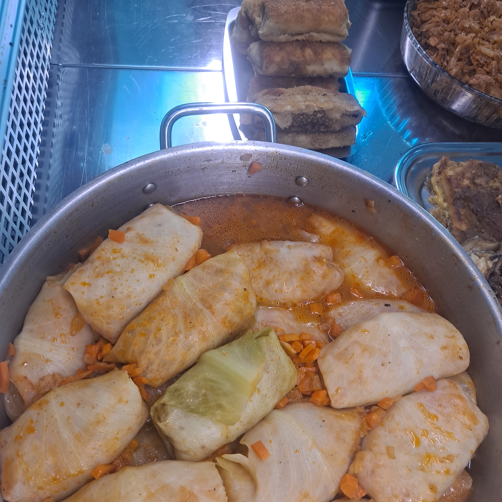 Gołąbki w sosie pomidorowym z marchewką, ułożone w dużym metalowym garnku, z widocznymi krokietami i kapustą duszoną w tle.