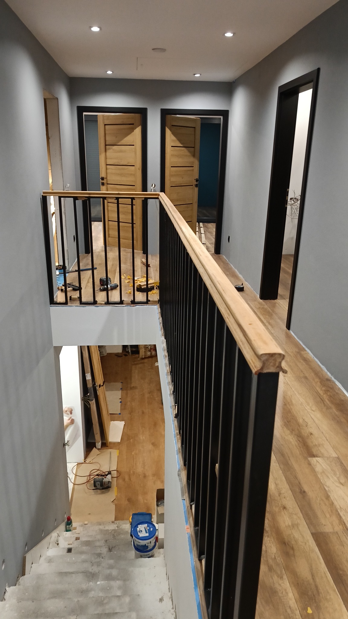 Wnętrze domu w trakcie remontu, widok na metalową balustradę z drewnianym poręczą, schody w stanie surowym i narzędzia na podłodze