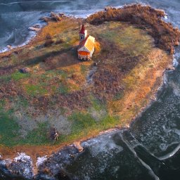 Malisz Film Studio - Widok z lotu ptaka na małą wyspę z kościołem, otoczoną częściowo zamarzniętym jeziorem.