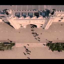 Malisz Film Studio - Szeroki kadr z lotu ptaka przedstawiający grupę ludzi wchodzących do budynku o architekturze zamkowej z jasnymi ścianami i szarym brukowanym placem.