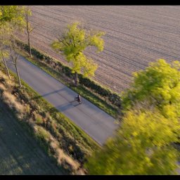 Malisz Film Studio - Ujęcie z drona przedstawiające motocyklistę jadącego asfaltową drogą, otoczoną polami i drzewami w jesiennej scenerii.