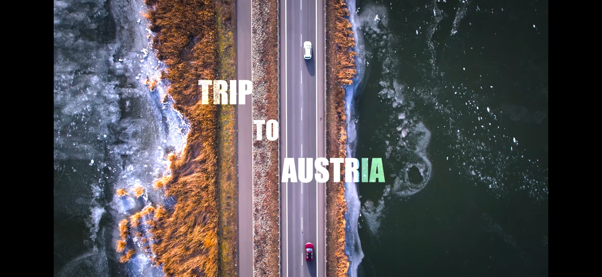 Widok z lotu ptaka na drogę w Austrii, obok zamarznięte jezioro i łąka, na drodze dwa samochody.