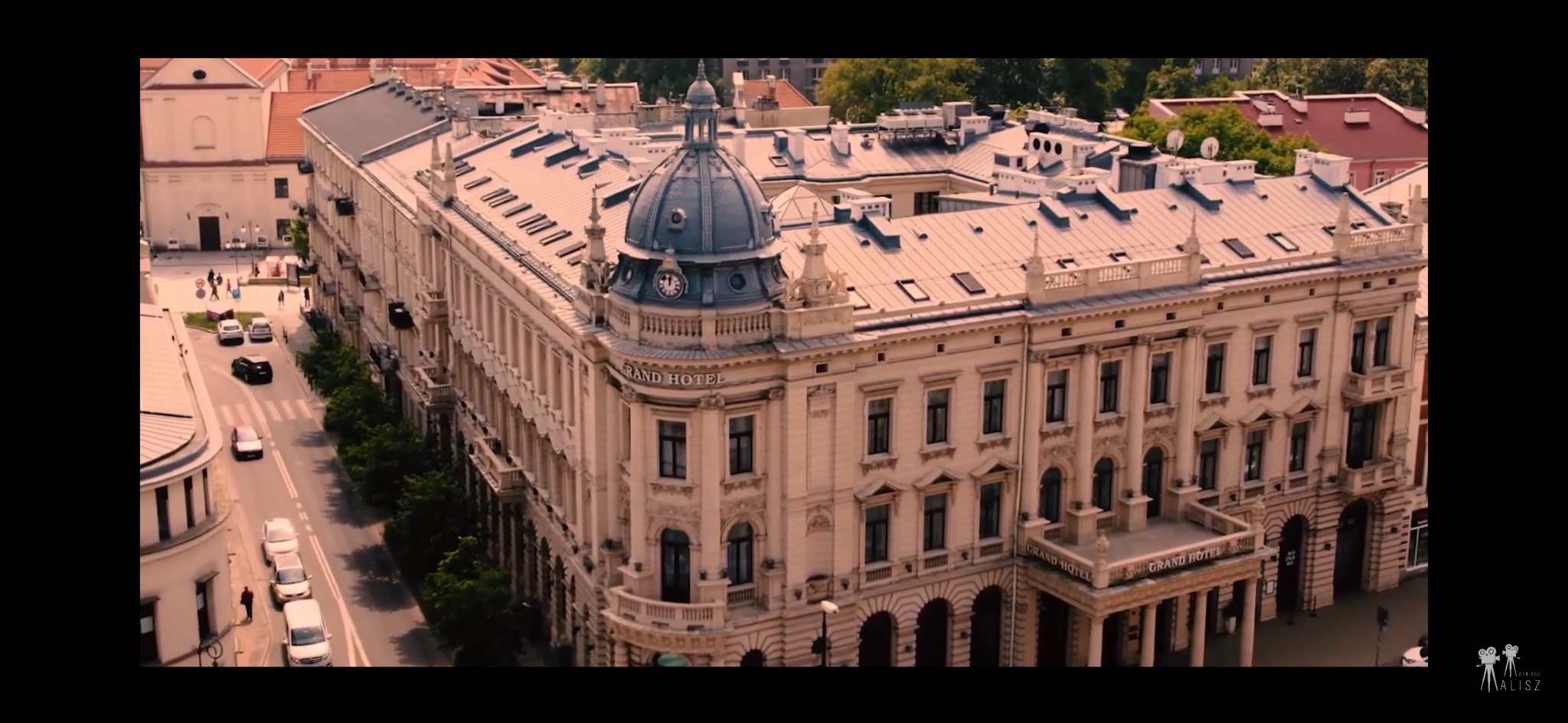 Elewacja Grand Hotelu z kopułą i zegarem, widok z góry na ulicę z samochodami i pieszymi.