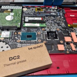 KMTechFix Kacper Wójcik - Otwarty laptop z widoczną płytą główną, dyskiem twardym, pamięcią RAM i kartą sieciową, obok pudełko pasty termoprzewodzącej 'be quiet! DC2 Thermal grease'.