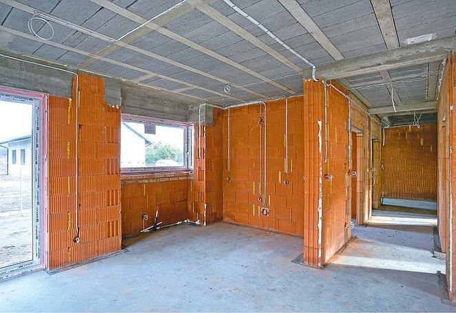 Surowy stan wnętrza budynku w Bydgoszczy z widocznymi przewodami elektrycznymi poprowadzonymi po ścianach z cegły ceramicznej.