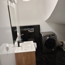 RIW remonty i wykończenia - Wykończona łazienka w stylu nowoczesnym z czarno-białymi płytkami imitującymi marmur, umywalką z szafką w kolorze drewna, pralką Samsung i oświetleniem punktowym nad lustrem.