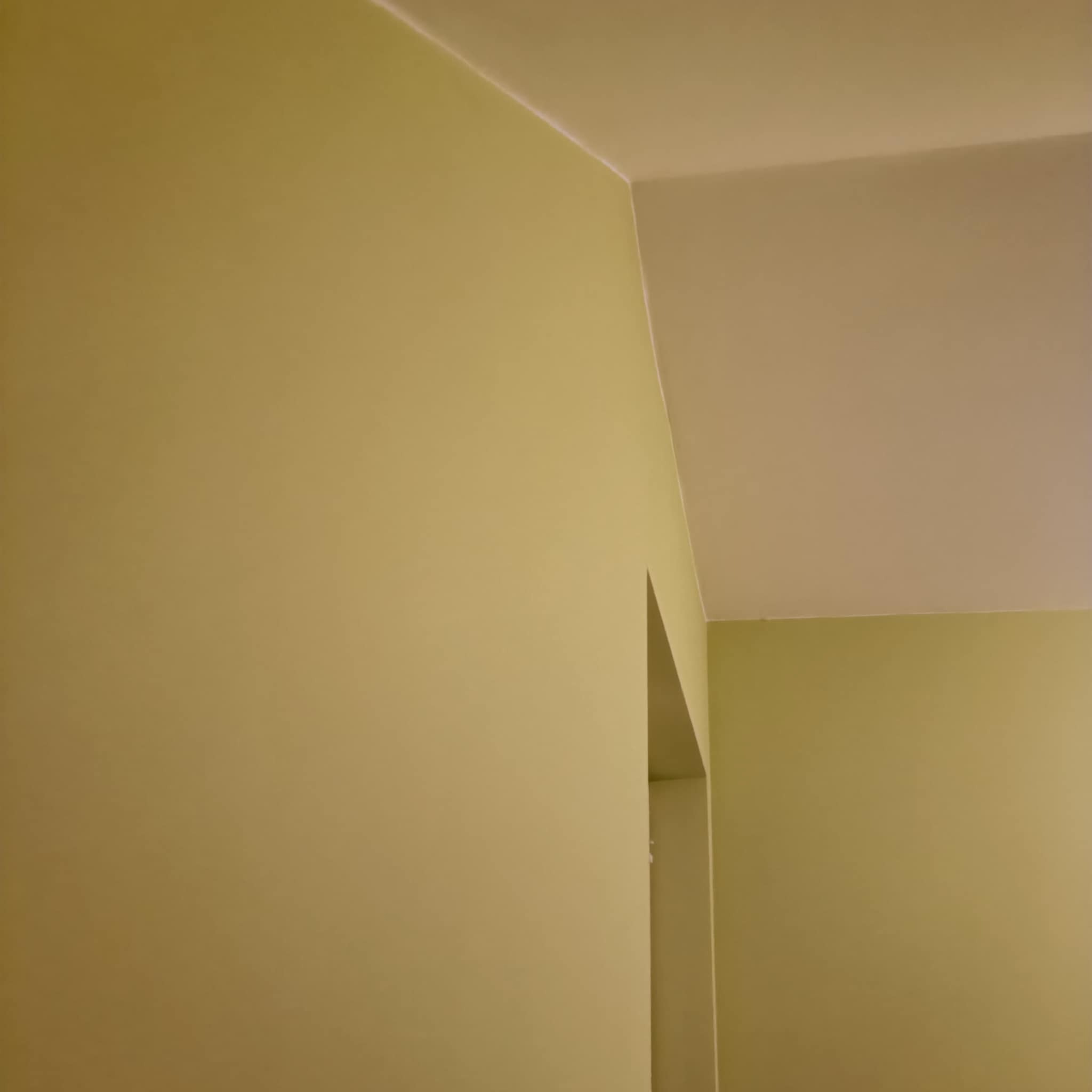 Pomarańczowo-żółta ściana świeżo po malowaniu, widoczny fragment sufitu i wnęka drzwiowa, proste linie łączenia ścian i sufitu.