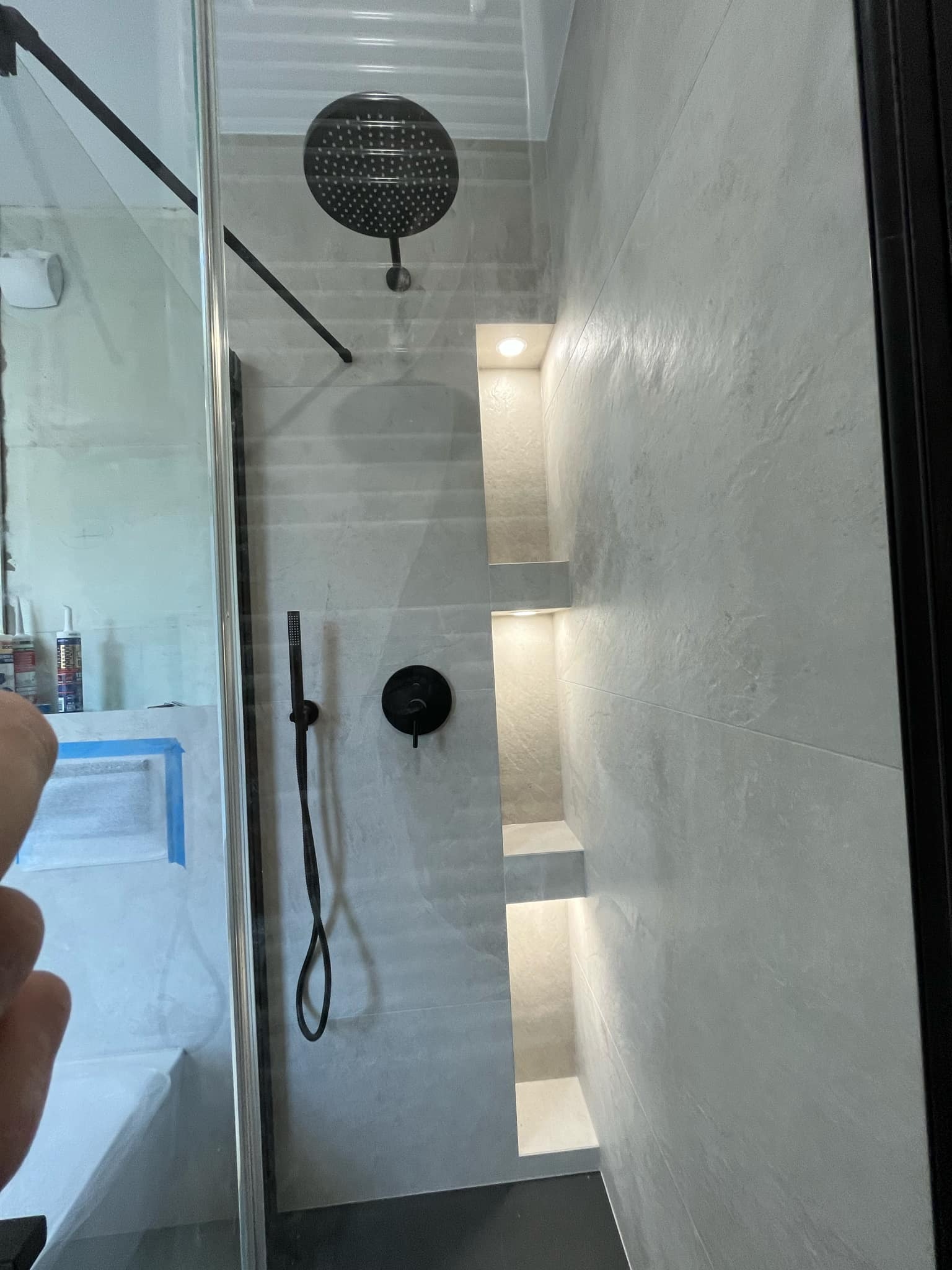 Wykończona kabina prysznicowa z czarną armaturą, wnękami z oświetleniem i szarą płytką imitującą beton.