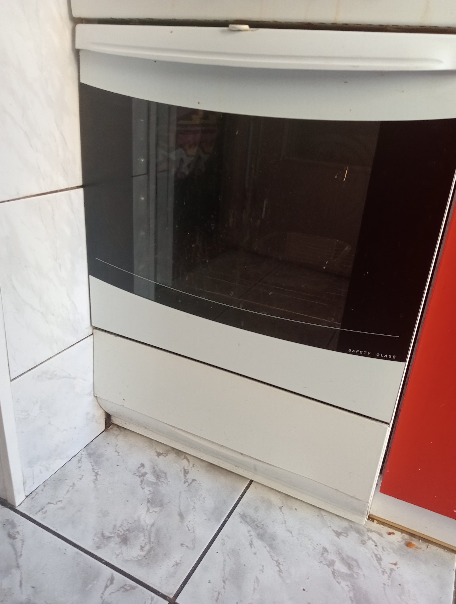 Brudny piekarnik z szybą Safety Glass oraz brudne płytki podłogowe i ścienne w kuchni przed sprzątaniem.