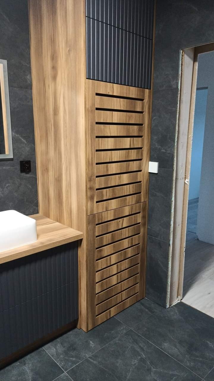 Nowoczesna łazienka z szafką z drewnianymi lamelami i szarą płytką imitującą kamień na ścianach i podłodze, widoczna umywalka nablatowa.