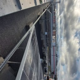 LENAR-BUD PRZEMYSŁAW GICZELA - Widok z góry na panele słoneczne z kroplami wody, zamontowane na dachu budynku z parkingiem i sklepem w tle pod zachmurzonym niebem.