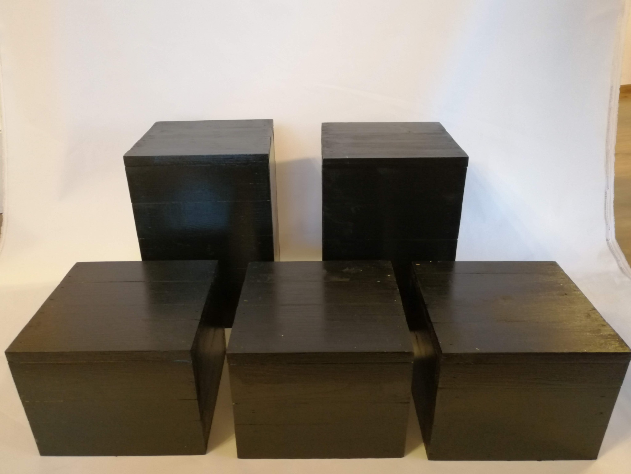 Pięć czarnych, drewnianych, lakierowanych kubików o różnej wysokości ustawionych na białym tle, mogących służyć jako elementy dekoracyjne lub ekspozytory.