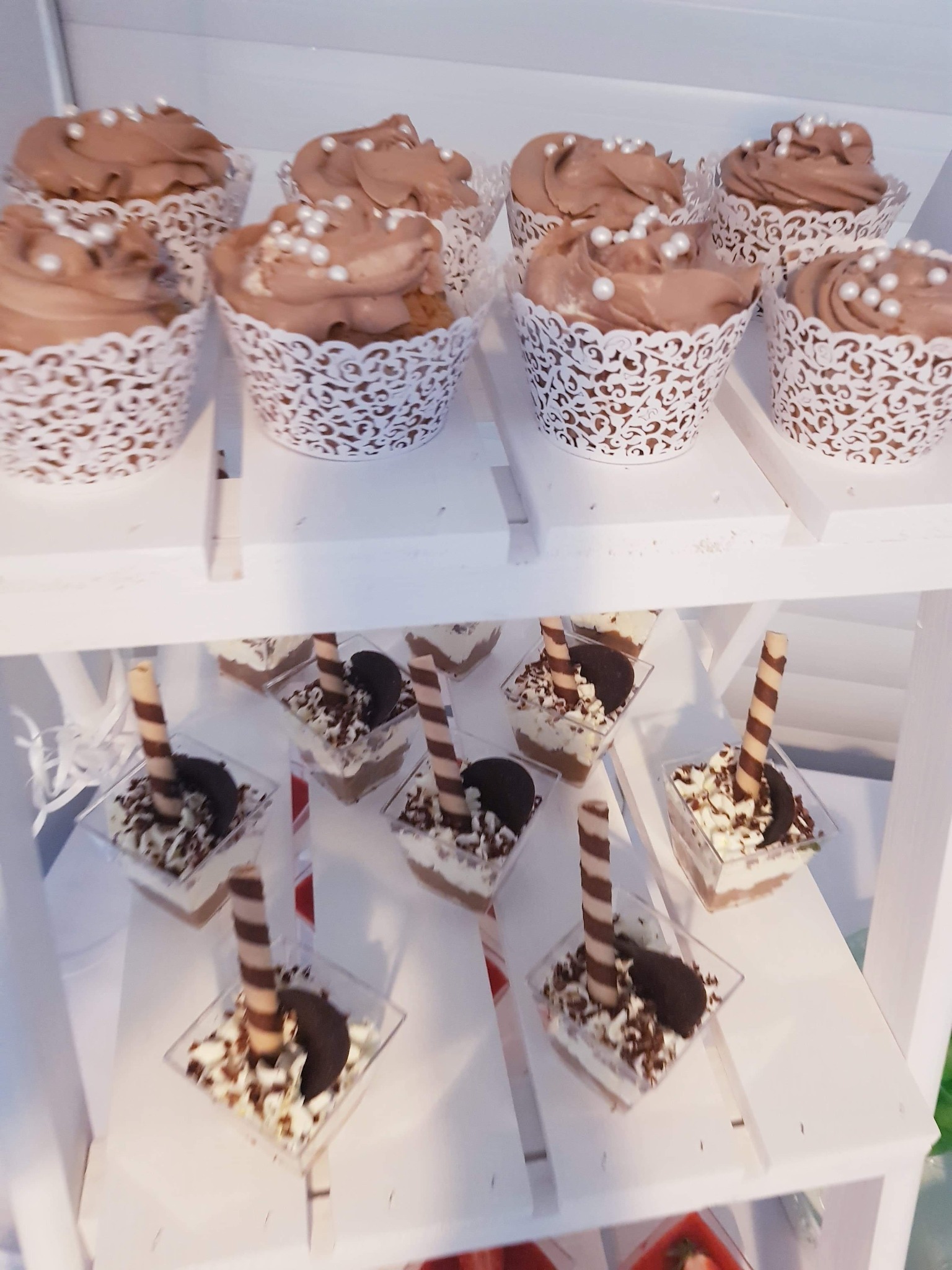 Deserowe babeczki z czekoladowym kremem i perłowymi kuleczkami oraz mini desery w kwadratowych plastikowych pojemnikach z kremem, posypką czekoladową, rurką waflową i ciasteczkiem Oreo, ułożone...