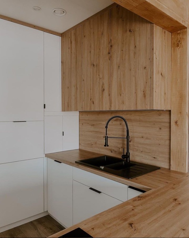 Nowoczesna kuchnia: białe szafki dolne i górne, drewnopodobne fronty szafek wiszących, czarny zlew z baterią ze sprężyną, drewniany blat.