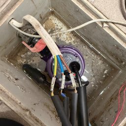 LuLu Instal Bohdan Pasevych - Podłączenie kabli do pompy zanurzeniowej w studzience. Widoczne przewody z kolorowymi izolacjami i czarne rury. Praca instalacyjna w szarej, betonowej studzience.