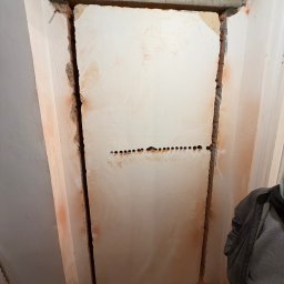 LuLu Instal Bohdan Pasevych - Wykute bruzdy w ścianie pod instalację elektryczną, widoczne otwory pod kable. Ściana w trakcie remontu, surowy beton nad otworem drzwiowym.