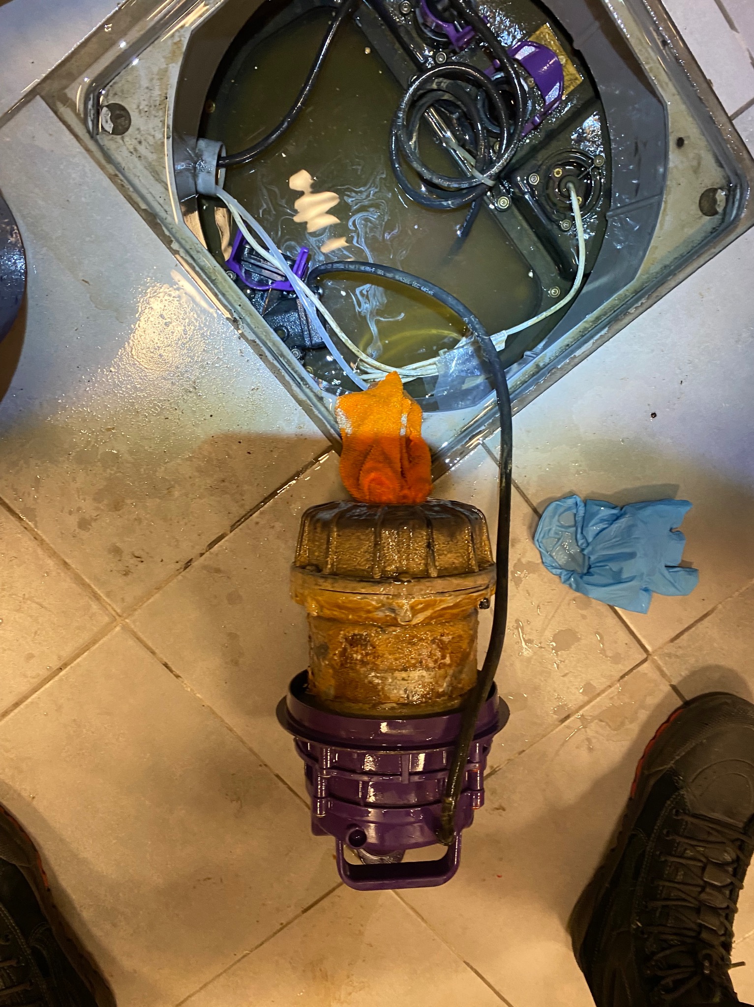 Oczyszczona pompa zanurzeniowa z elementami instalacji w studzience, widoczne przewody i akcesoria. Obok leżą rękawice ochronne i fragment buta.