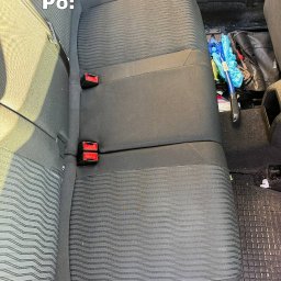 Tamara - Wyczyszczona tylna kanapa samochodu z ciemną tapicerką w prążki, widoczne czerwone zapięcia pasów, na podłodze leżą narzędzia i brudna wycieraczka.