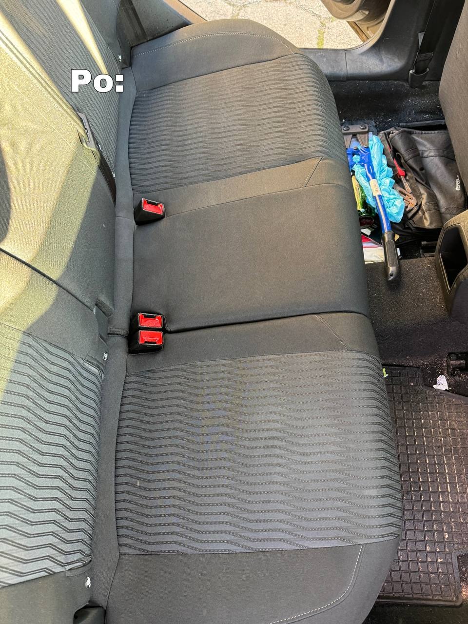 Wyczyszczona tylna kanapa samochodu z ciemną tapicerką w prążki, widoczne czerwone zapięcia pasów, na podłodze leżą narzędzia i brudna wycieraczka.