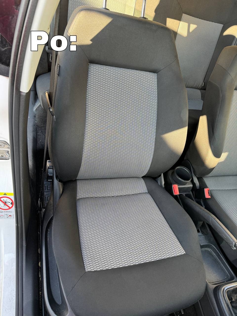 Wyraźne zbliżenie na wyczyszczone, szare siedzenie samochodowe z tkaniny w czarnych obramowaniach, widoczne elementy wnętrza pojazdu, po prawej stronie pas bezpieczeństwa, po lewej ostrzeżenie...