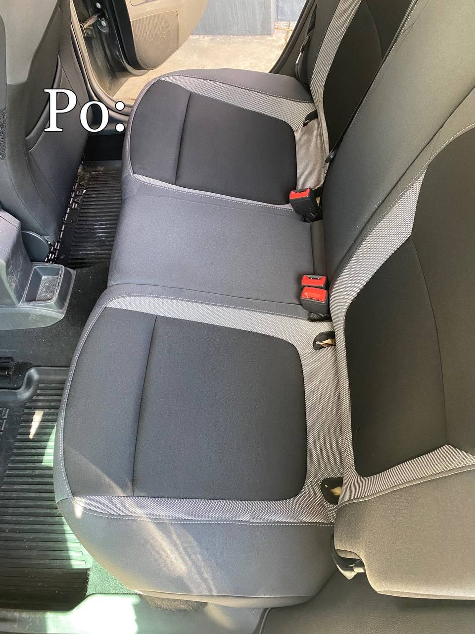 Wnętrze samochodu po czyszczeniu: tylna kanapa z czarnymi i szarymi pokrowcami, widoczne pasy bezpieczeństwa z czerwonymi elementami, czysta gumowa wycieraczka pod nogami.