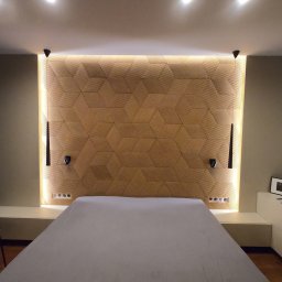 MACIEJ MATYSIAK - Sypialnia z podświetlanym panelem dekoracyjnym z geometrycznym wzorem nad łóżkiem, minimalistyczne lampki ścienne i stolik nocny z dekoracjami.