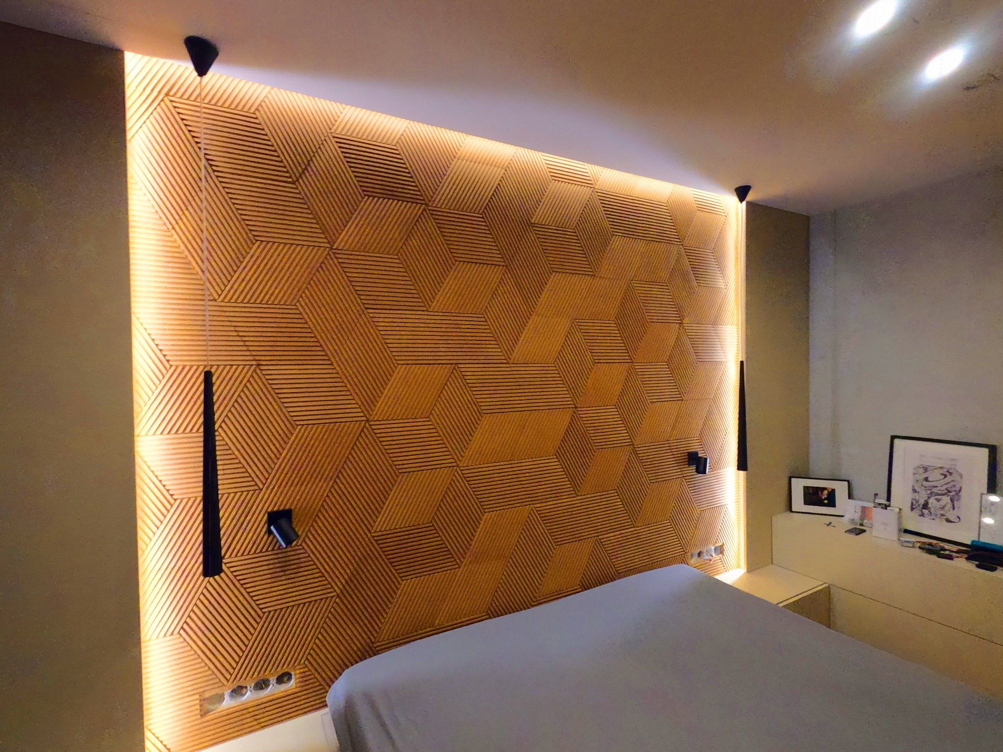 Nowoczesna sypialnia z drewnianą ścianą dekoracyjną z geometrycznym wzorem, podświetloną listwami LED, czarne lampki ścienne, łóżko z szarą pościelą, biała szafka nocna z dekoracjami.