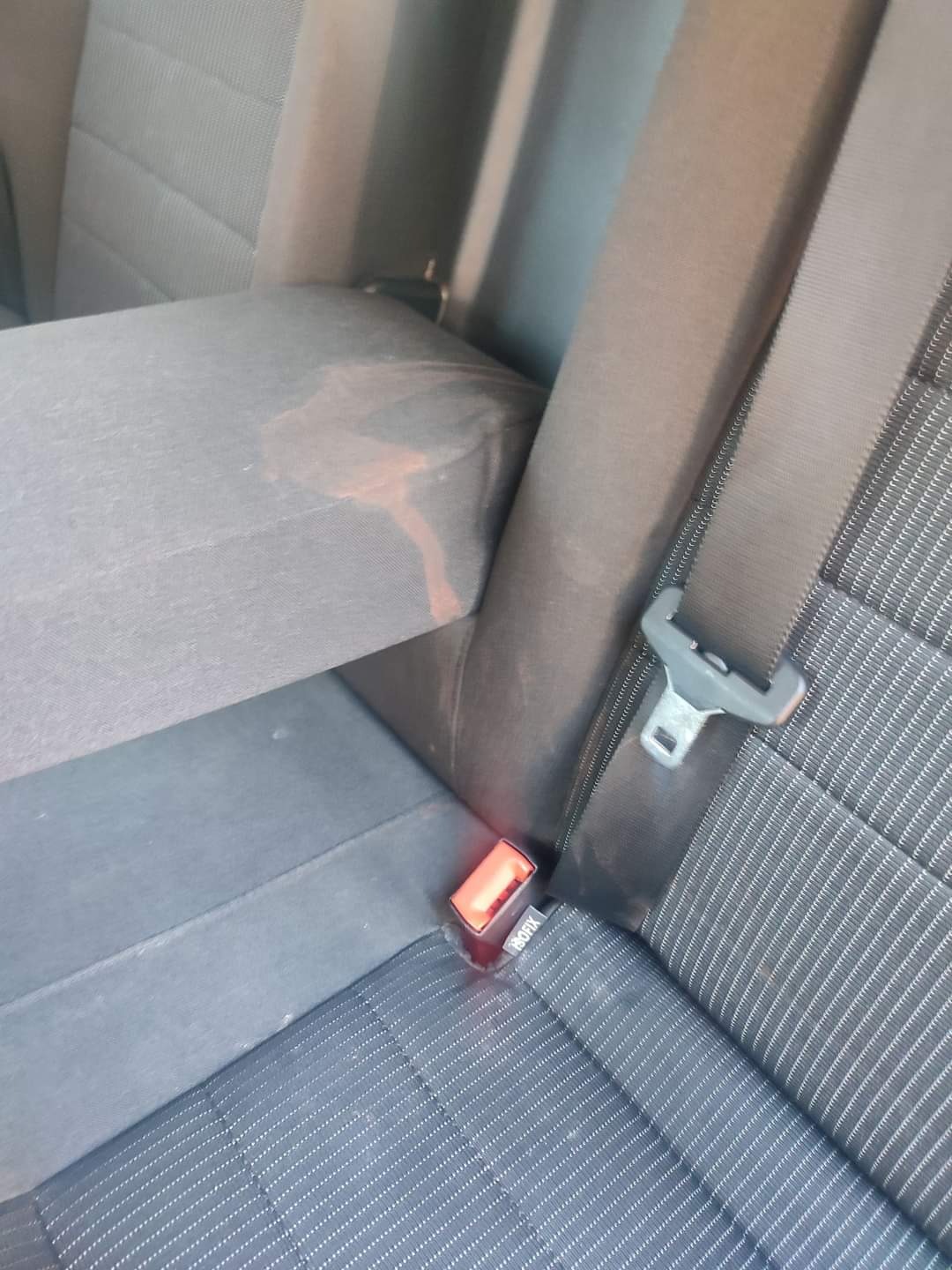 Brudna, poplamiona tapicerka na tylnym siedzeniu samochodu z widocznym zapięciem pasa bezpieczeństwa.