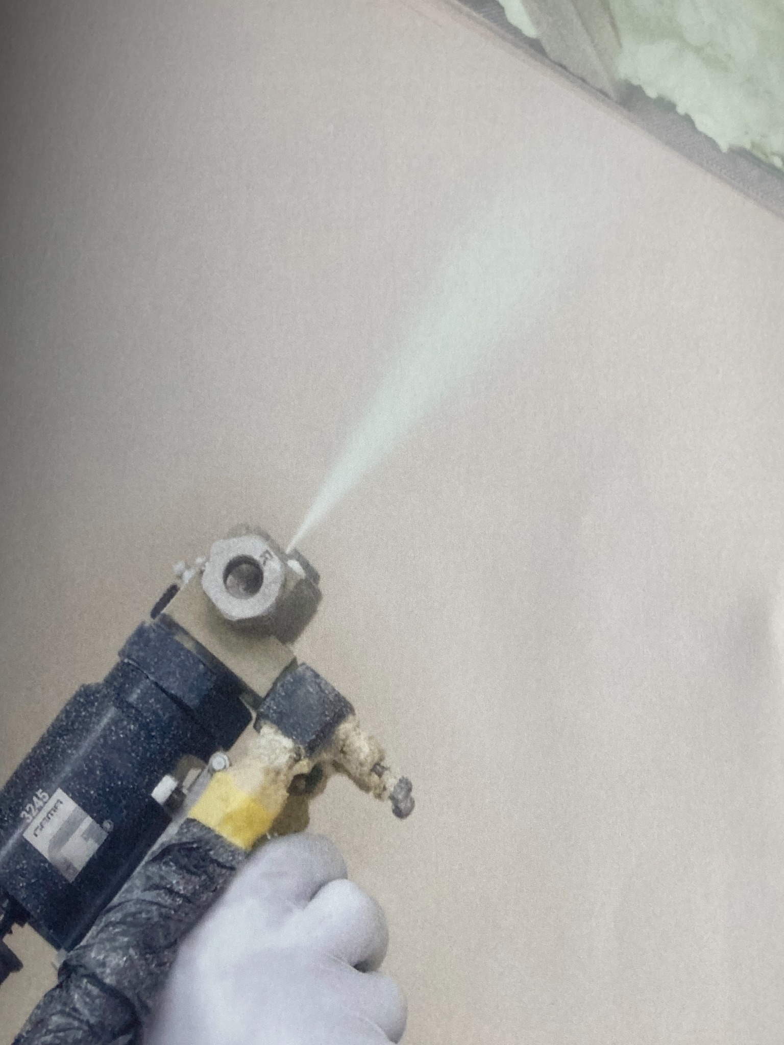 Natrysk pianki PUR na ścianę z bliska, widoczny pistolet aplikacyjny i dłoń w rękawicy. W tle ocieplona powierzchnia.