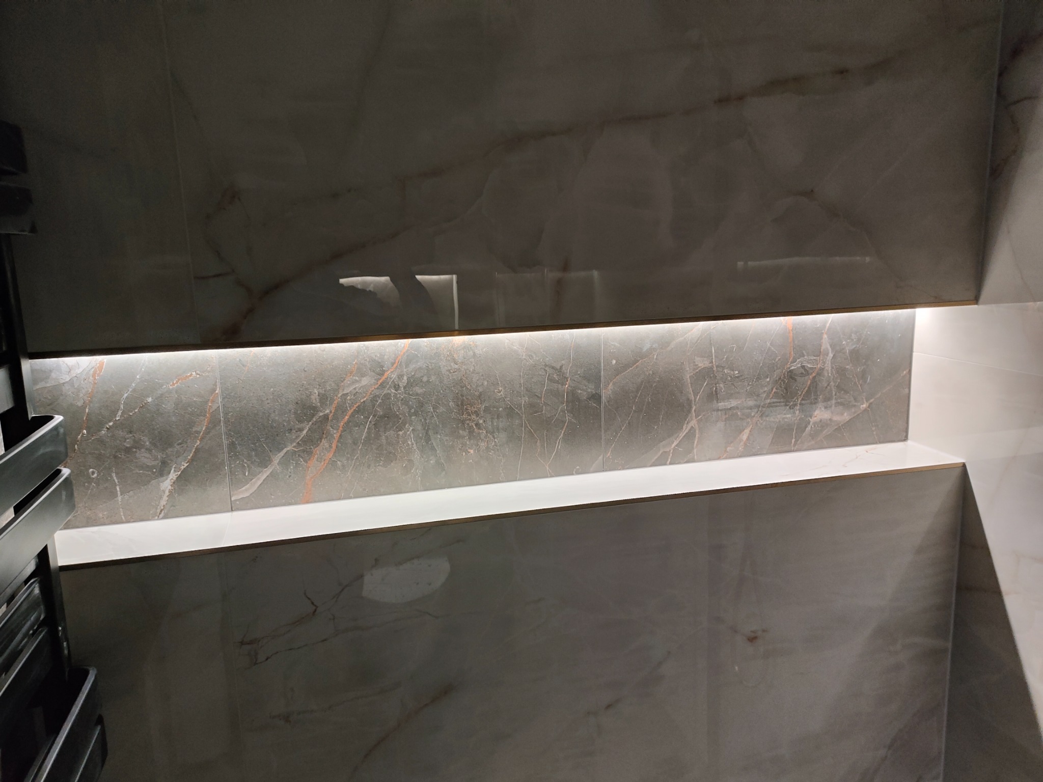 Półka z podświetleniem LED w łazience, wykończona płytkami imitującymi marmur. Nowoczesny design, ciepłe światło, subtelne detale wykończenia.