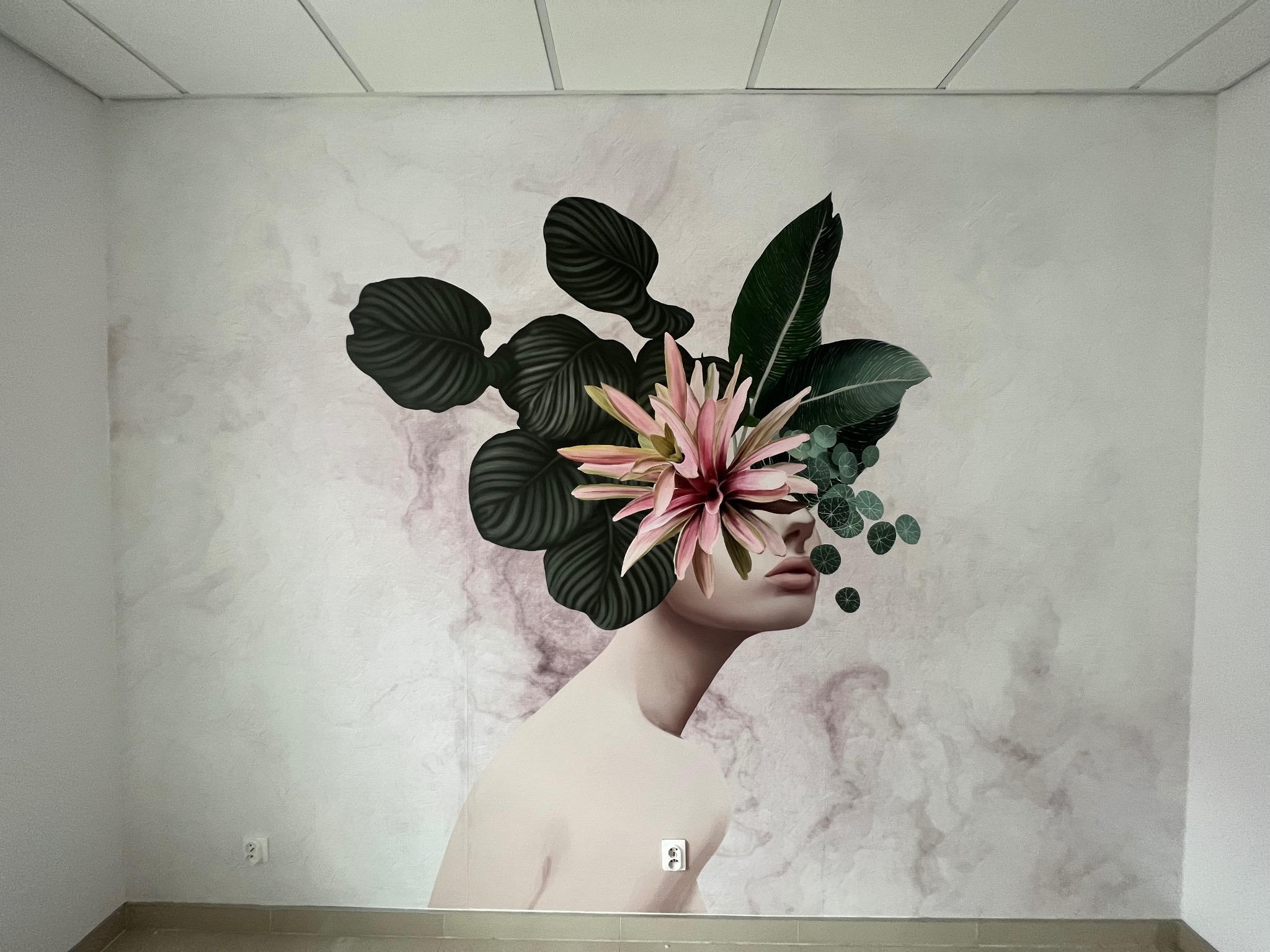 Malowidło ścienne przedstawiające profil kobiety z kwiatami i liśćmi zamiast włosów, na ścianie o teksturze marmuru, widoczny kontakt elektryczny w dolnej części.