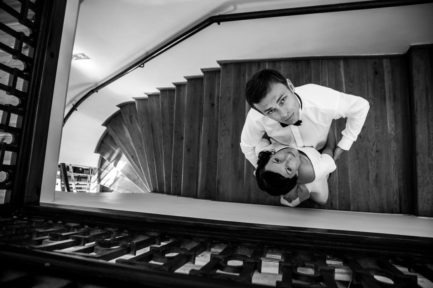 Czarno-białe zdjęcie z góry przedstawiające parę młodą stojącą na drewnianych schodach, widoczne ozdobne metalowe barierki w dolnej części kadru.